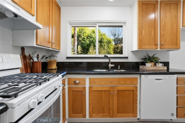 kitchen with white appliances, a sink, exhaust hood, brown cabinetry, and dark stone countertops