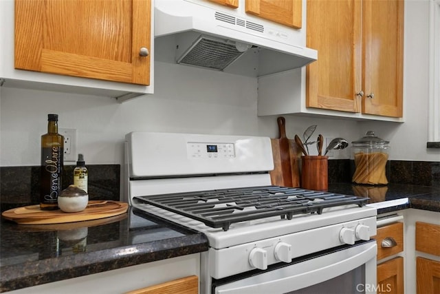 kitchen with dark stone counters, brown cabinets, white range with gas cooktop, and under cabinet range hood