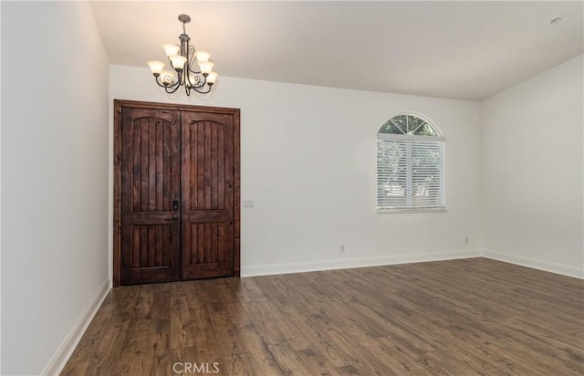 empty room with a chandelier, baseboards, and wood finished floors