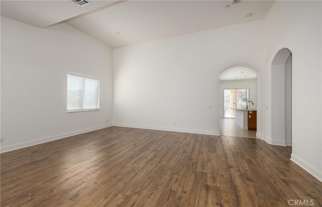 spare room with arched walkways, a healthy amount of sunlight, dark wood finished floors, and baseboards