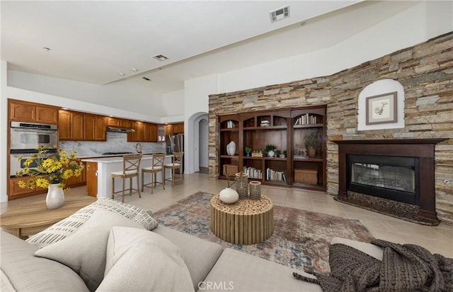 living room featuring arched walkways, visible vents, a glass covered fireplace, and light tile patterned floors