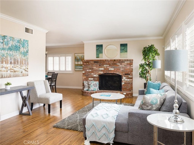 living room featuring baseboards, visible vents, wood finished floors, crown molding, and a brick fireplace