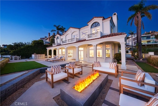 back of property featuring an outdoor living space with a fire pit, a balcony, a patio, a tiled roof, and french doors