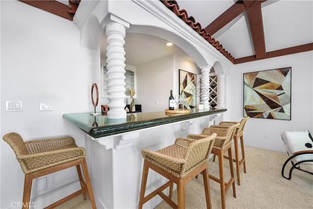 bar featuring arched walkways, beamed ceiling, carpet flooring, a bar, and ornate columns