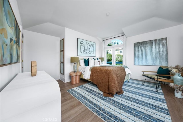 bedroom with vaulted ceiling, wood finished floors, and baseboards