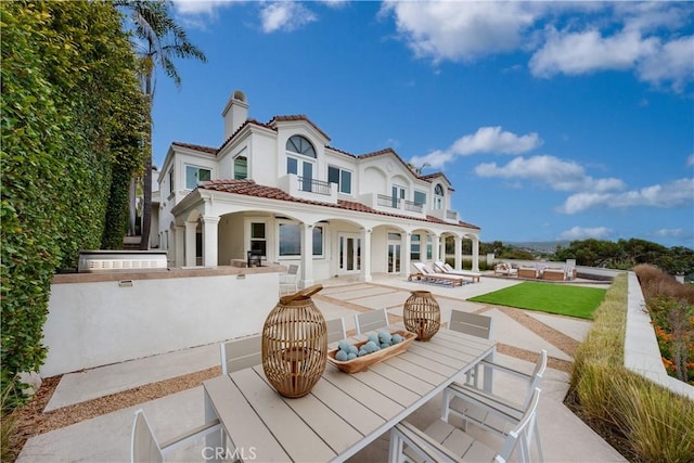 rear view of property featuring a balcony, a tile roof, french doors, a chimney, and a patio area