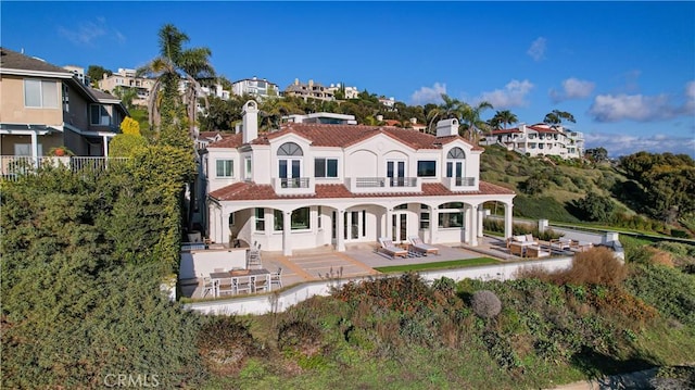 rear view of property featuring a patio, a balcony, a tile roof, a chimney, and stucco siding