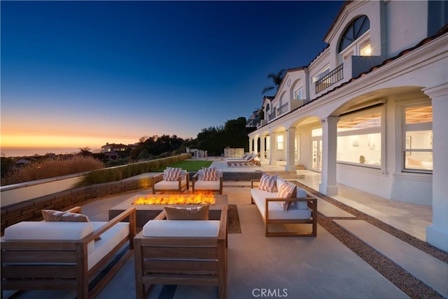 patio terrace at dusk featuring an outdoor living space with a fire pit and a balcony