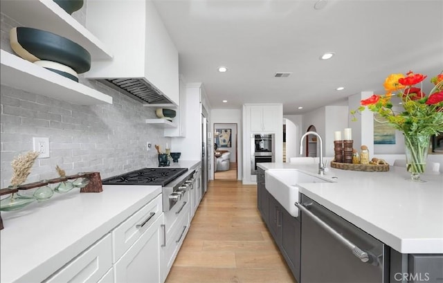 kitchen with light wood-style flooring, stainless steel appliances, a sink, white cabinetry, and light countertops