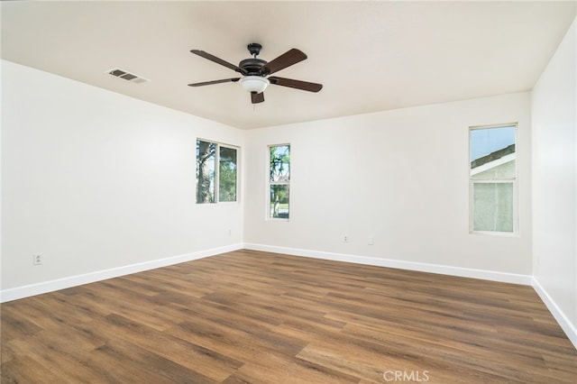 unfurnished room featuring dark wood-style floors, a ceiling fan, visible vents, and baseboards