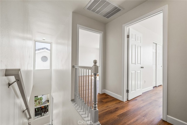 hallway with baseboards, visible vents, dark wood-style flooring, and an upstairs landing