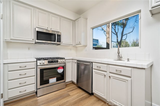 kitchen with white cabinets, tile countertops, light wood-style flooring, stainless steel appliances, and a sink