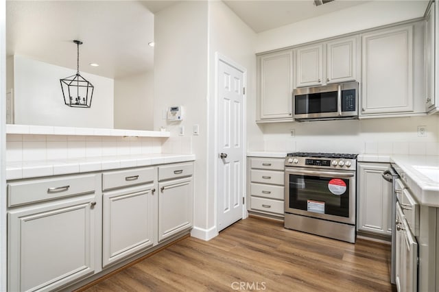 kitchen with tile countertops, wood finished floors, hanging light fixtures, stainless steel appliances, and gray cabinetry