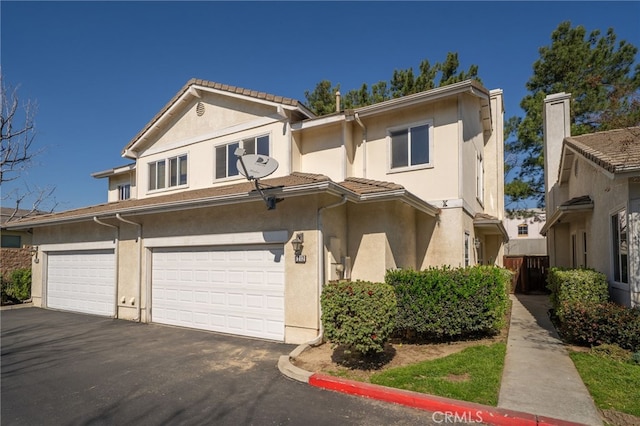 view of front facade featuring an attached garage, a tile roof, aphalt driveway, and stucco siding