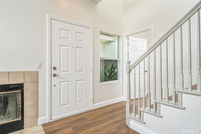 foyer entrance featuring stairs, a tile fireplace, wood finished floors, and baseboards