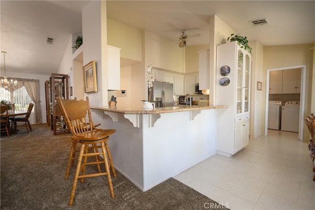 kitchen featuring visible vents, a kitchen bar, stainless steel fridge, washing machine and clothes dryer, and ceiling fan with notable chandelier