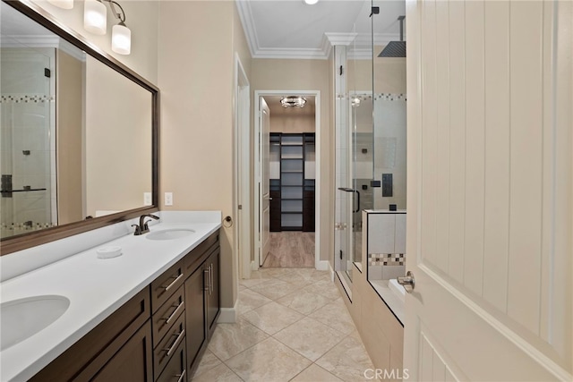 bathroom with a spacious closet, a stall shower, a sink, and crown molding