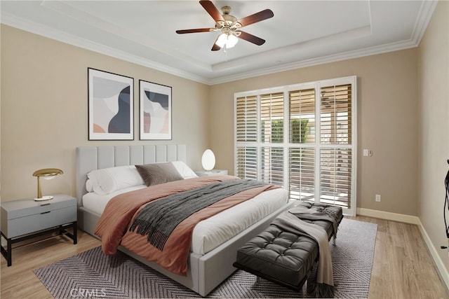 bedroom featuring crown molding, a raised ceiling, ceiling fan, light wood-type flooring, and baseboards