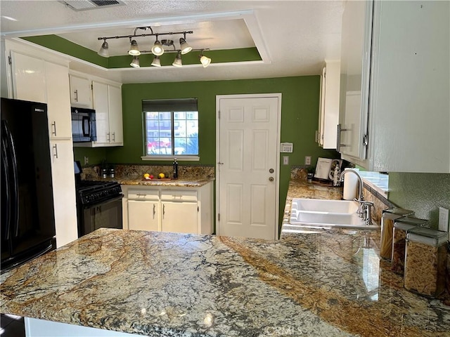 kitchen with a raised ceiling, a peninsula, black appliances, white cabinetry, and a sink