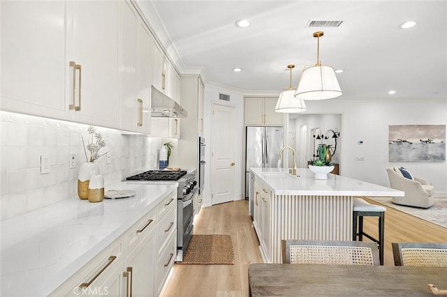 kitchen featuring a breakfast bar area, light wood-style flooring, under cabinet range hood, appliances with stainless steel finishes, and decorative backsplash