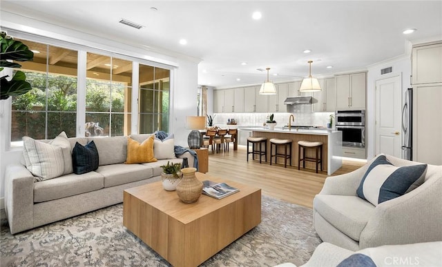 living room featuring ornamental molding, light wood-type flooring, visible vents, and recessed lighting