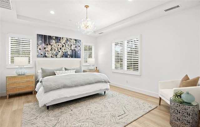 bedroom with light wood-style floors, a raised ceiling, visible vents, and a notable chandelier