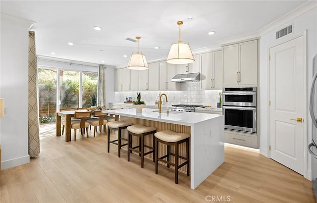 kitchen featuring double oven, under cabinet range hood, visible vents, light countertops, and backsplash