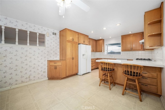 kitchen featuring a peninsula, white refrigerator with ice dispenser, a breakfast bar, light countertops, and wallpapered walls