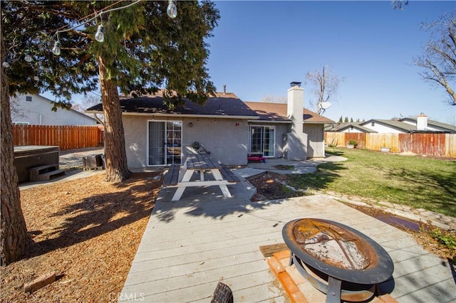 rear view of property featuring a hot tub, a fire pit, a fenced backyard, a chimney, and a deck