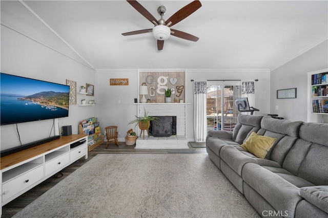 living area featuring dark wood finished floors, ceiling fan, vaulted ceiling, crown molding, and a fireplace