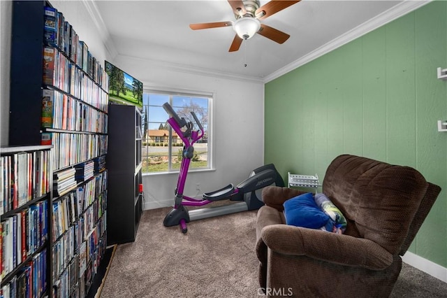 sitting room with carpet, crown molding, a ceiling fan, wall of books, and baseboards