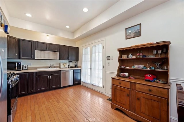 kitchen with wainscoting, stainless steel appliances, light countertops, light wood-style floors, and a sink