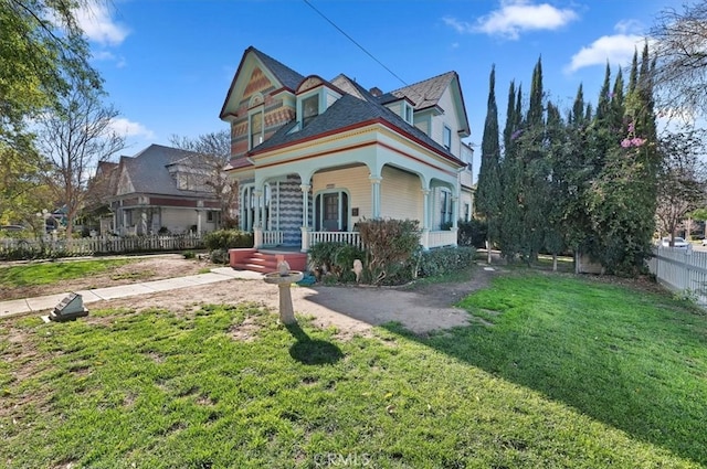 victorian home featuring covered porch, fence, and a front lawn