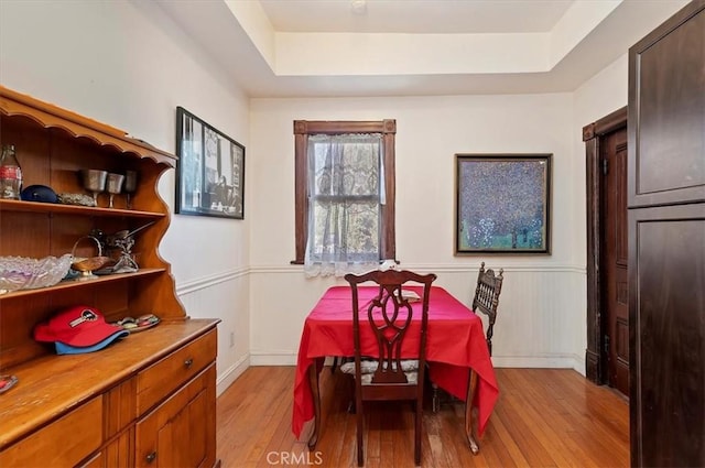 dining room with a tray ceiling, a wainscoted wall, and light wood-style flooring