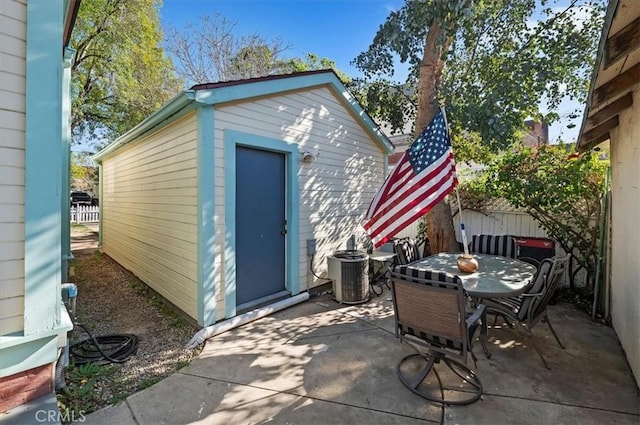 view of outdoor structure featuring central air condition unit, outdoor dining space, fence, and an outbuilding