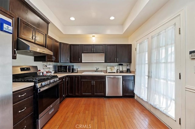 kitchen with stainless steel appliances, light countertops, a sink, and under cabinet range hood