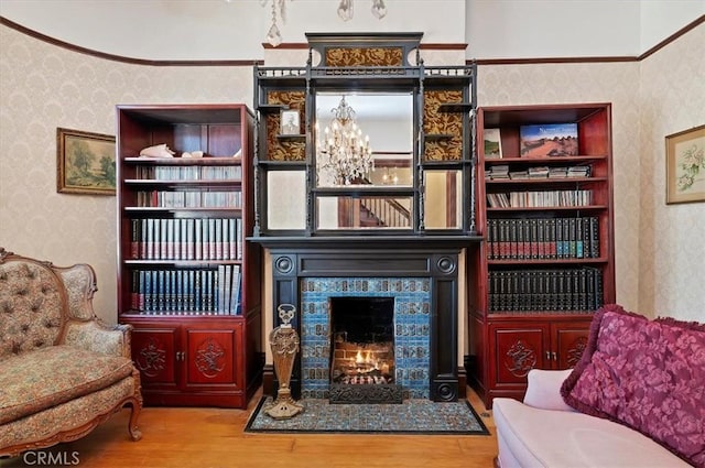 sitting room featuring a warm lit fireplace, a notable chandelier, wood finished floors, and wallpapered walls