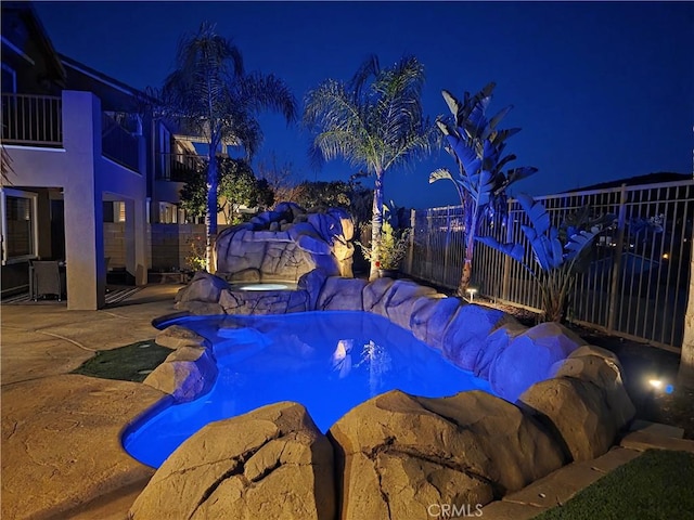 pool at night featuring a fenced in pool, fence, and an in ground hot tub