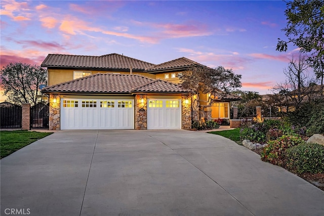 mediterranean / spanish-style house with a garage, concrete driveway, stone siding, a tile roof, and fence