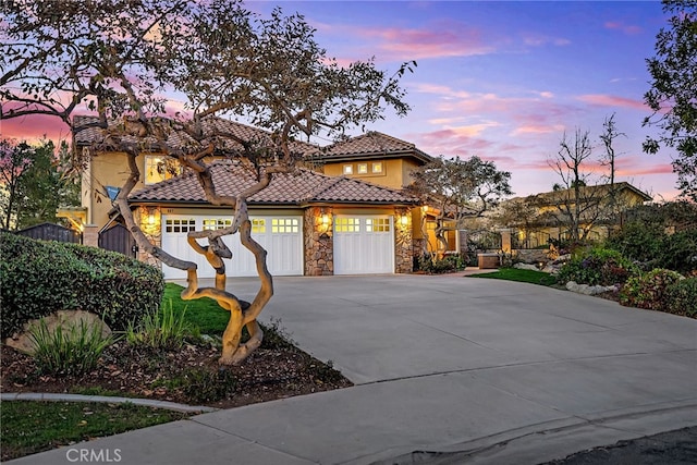 mediterranean / spanish-style house featuring an attached garage, concrete driveway, stone siding, a tiled roof, and stucco siding