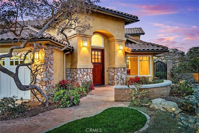 doorway to property with stone siding, a tile roof, fence, and stucco siding