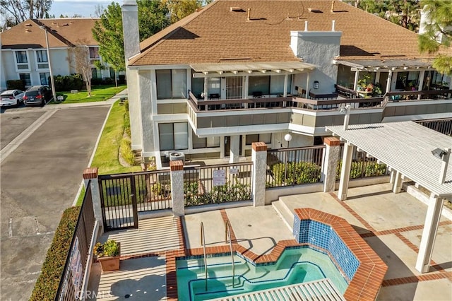 rear view of property with a chimney, a shingled roof, a community hot tub, a balcony, and a residential view