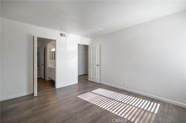 unfurnished bedroom featuring ensuite bath, baseboards, visible vents, and dark wood-style flooring