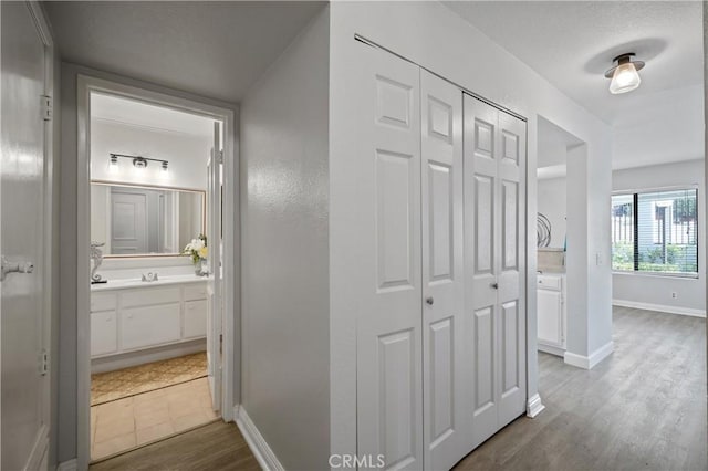 hall featuring a sink, baseboards, and dark wood-style flooring