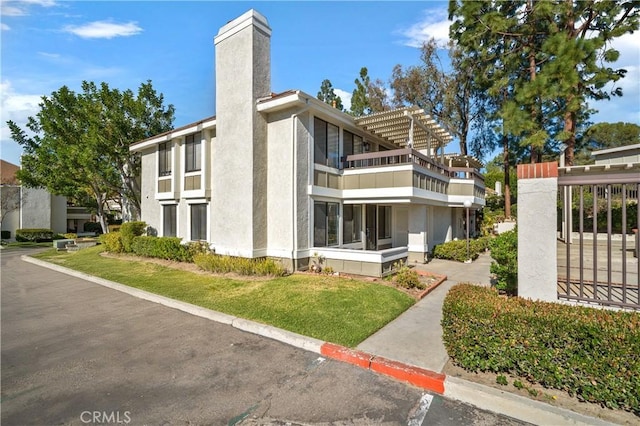 view of side of property with a chimney, a balcony, a lawn, and stucco siding