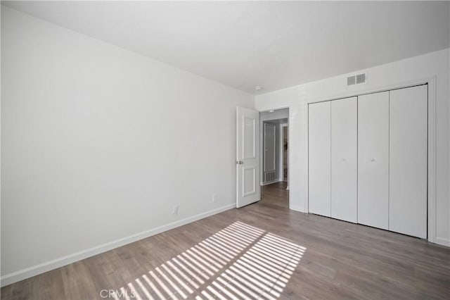 unfurnished bedroom featuring a closet, visible vents, baseboards, and wood finished floors