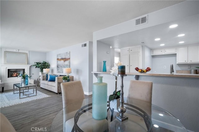 dining room with recessed lighting, a warm lit fireplace, visible vents, and wood finished floors