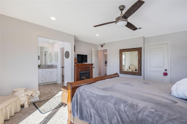 bedroom featuring a ceiling fan, a glass covered fireplace, connected bathroom, and recessed lighting