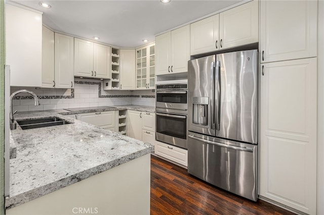 kitchen featuring light stone counters, backsplash, appliances with stainless steel finishes, glass insert cabinets, and a sink