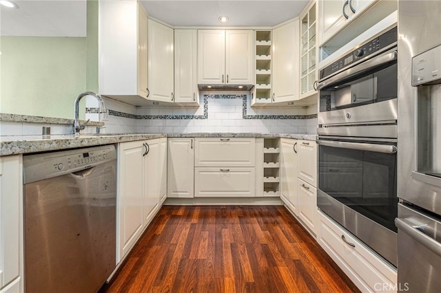 kitchen featuring light stone counters, dark wood finished floors, tasteful backsplash, appliances with stainless steel finishes, and white cabinetry